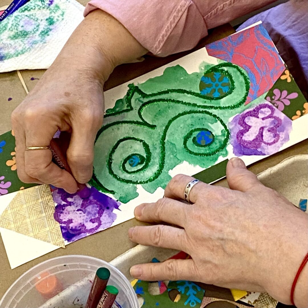 Hands painting a colorful floral design on paper.