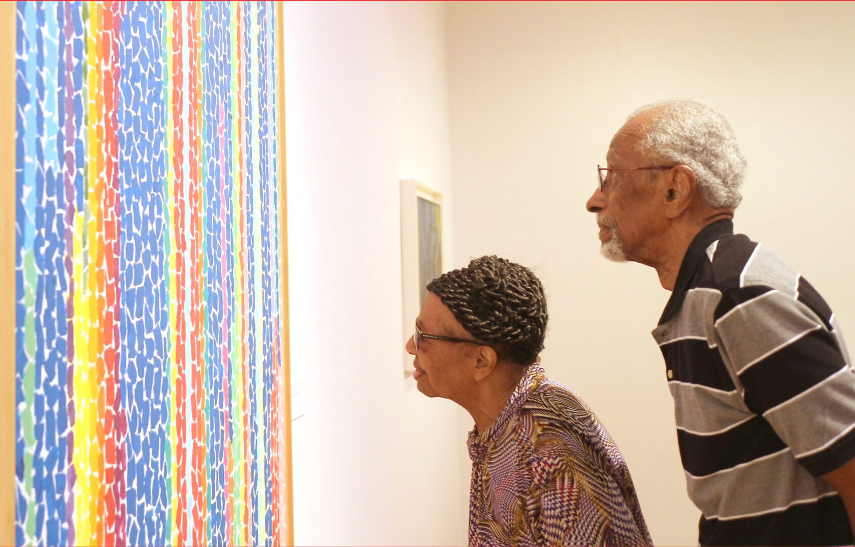Two elderly individuals closely examining colorful art in a gallery.