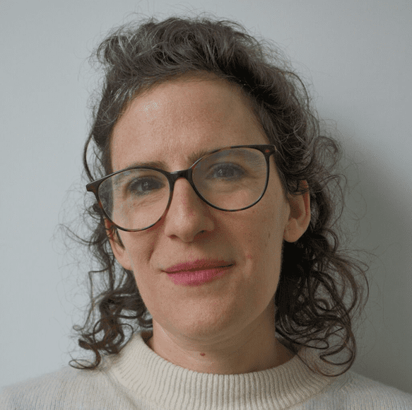 Portrait of a woman with glasses and curly hair against a plain background.