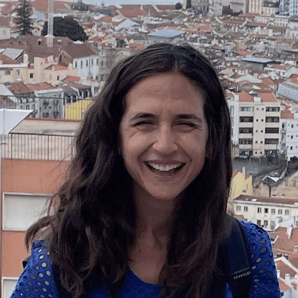 Smiling woman with long dark hair outdoors in a city setting.