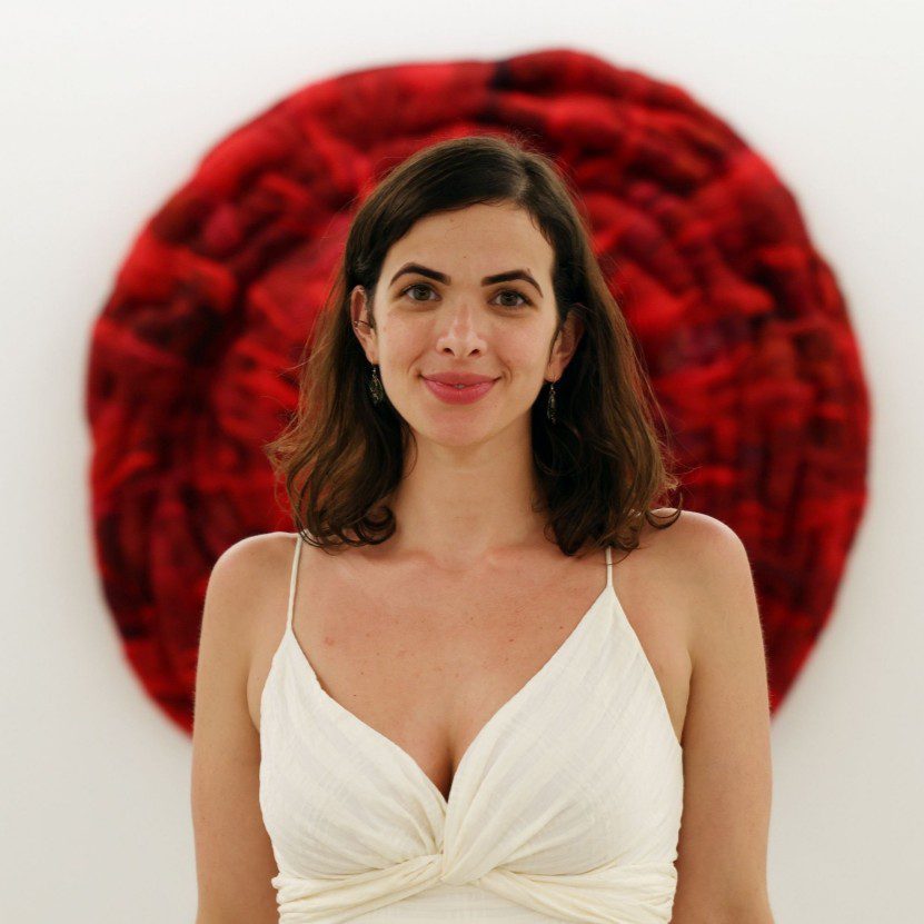 Woman in white dress stands before a red circular artwork.