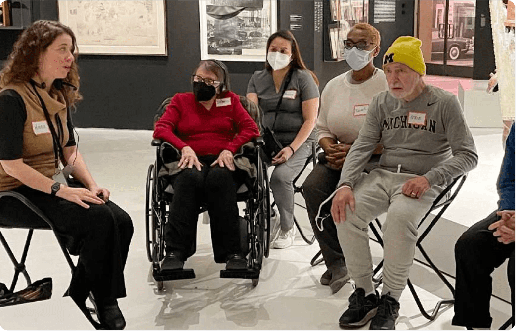 People in wheelchairs and others wearing face masks in a gallery setting.