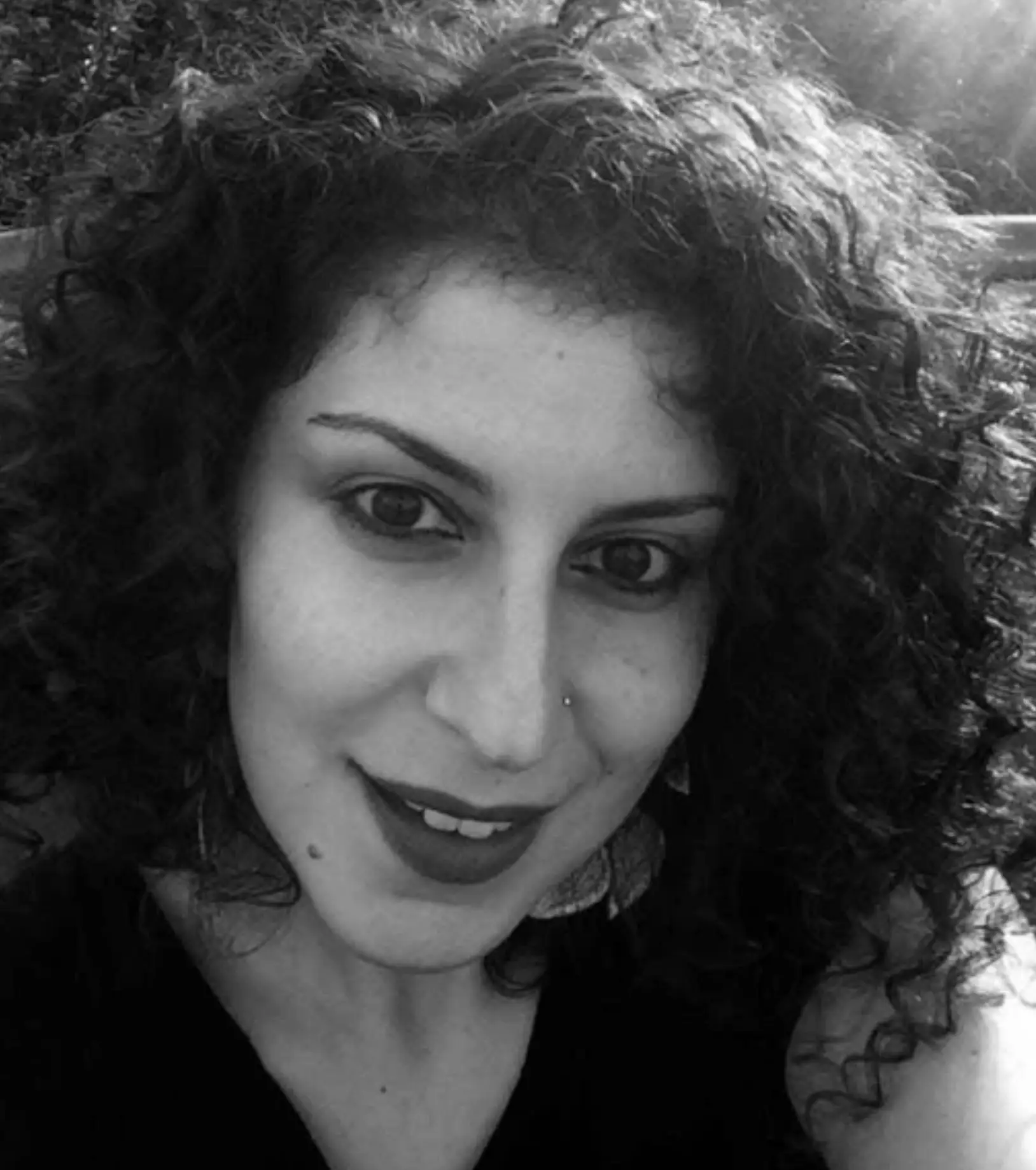 Smiling person with curly hair, black and white.